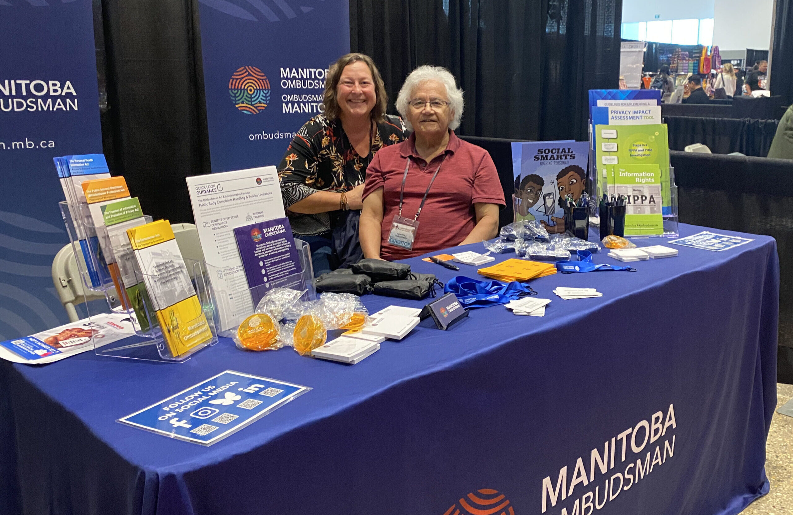 Two ombudsman office staff at an educational booth featuring banners and print materials about the office.